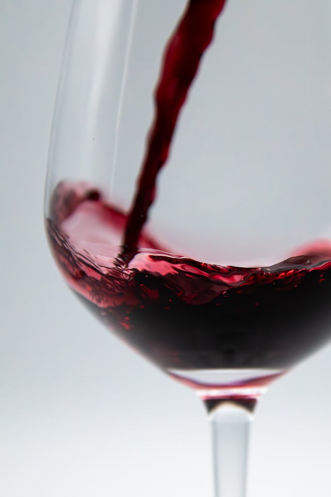 Captivating close-up of red wine being poured into a glass on a white background.
